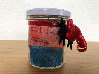 Barattolo da conserva sigillato con un'etichetta dipinta con la scritta “Per papà da Anahí” scritta a mano dai bambini. Il barattolo è decorato con un nastro.