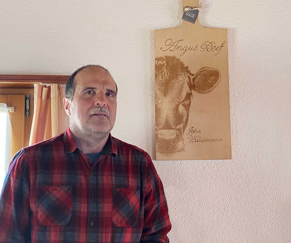 Primo piano di John Haldemann davanti a una tavola di legno su cui è incisa una testa di Angus.