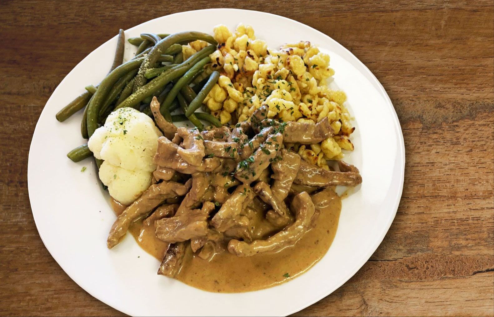 Carne affettata in salsa di senape servita con fagiolini, cavolfiore e spaetzli.