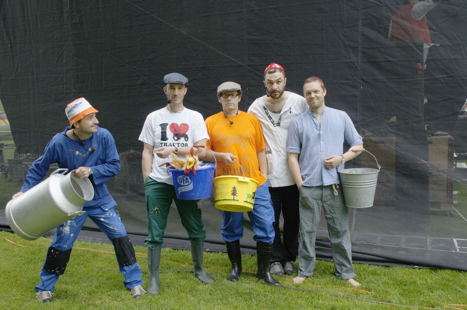 Andrew Bond mit seiner Band bei einem Auftritt, alle in Stallkleidern und mit Milchkann oder Eimer ausgerüstet.